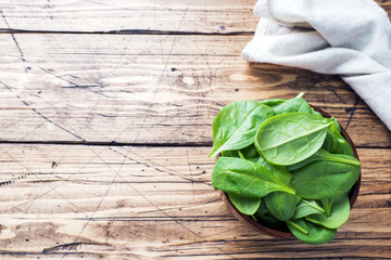 Fresh spinach leaves in bowl on rustic wooden table. Copy space