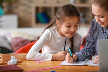 Cute girl with mother doing homework at home