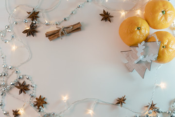 Orange mandarins, cinnamon sticks, anise stars and wooden tree toy on the wooden background with garlands