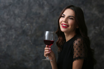 Beautiful young woman with glass of wine on dark background