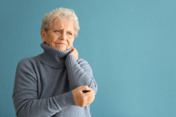 Senior woman suffering from pain in elbow on color background - obrazy, fototapety, plakaty