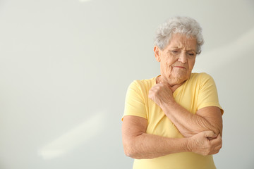 Senior woman suffering from pain in elbow on light background
