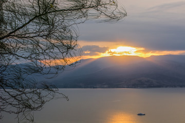 seascape sunset romantic atmosphere landscape with with soft focus on tree bare branches and unfocused mountain shape silhouette with evening sun rays light from behind ridge 