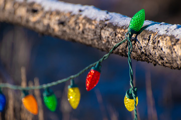 A string of colorful holiday lights decorate a snow-covered wooden fence