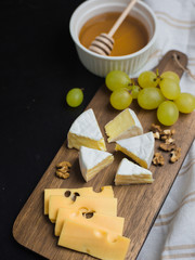 Slice of cheese, nuts, honey and grapes on wooden cutting board. Camembert cheese and edam cheese with plaid fabric. Food for wine and romantic