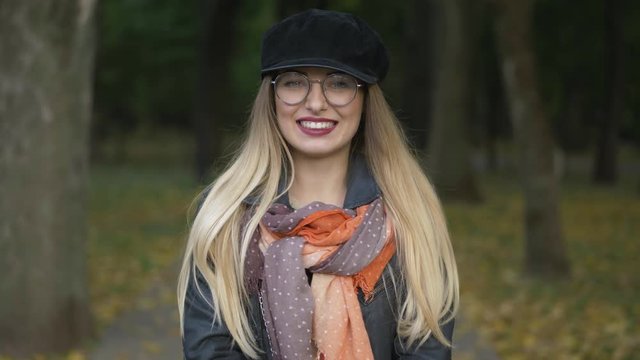 Young adorable blonde woman having fun at city park cold season, smiling into the camera. Close up, shallow depth of field.