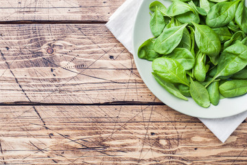 Fresh spinach leaves in bowl on rustic wooden table. Copy space