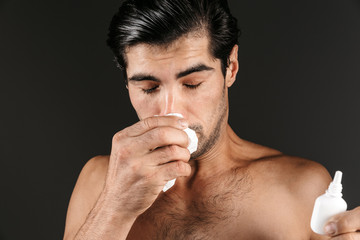 Ill young man posing isolated over dark wall background holding nasal spray bottle with napkin.