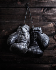 pair of very old shabby black leather boxing gloves hanging on a nail