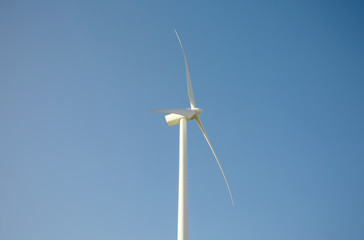 Closeup of windmill turbine and blades generating electricity over a blue sky background. Clean and ecological energy production concept.