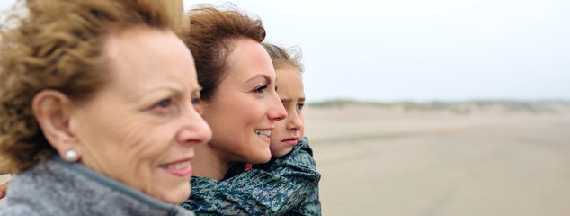 Closeup of three generations female looking at sea on the beach in autumn. Background focus on...