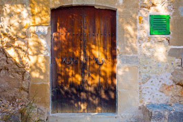 Brown old door and small green shutter on old traditional stone house in Majorca Spain