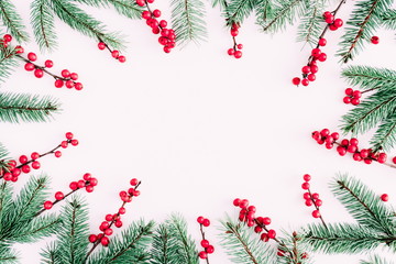 Christmas modern composition. Frame made of green fir tree branches and red berries on pastel pink background. Christmas, New Year, winter concept. Flat lay, top view, copy space