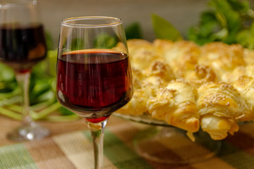 Homemade pastry with sesame and cheese and glass of wine of blackberry. Table with vintage bamboo mat and liana vine in the background.