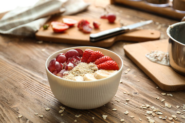 Bowl with tasty oatmeal, fruits and strawberry on wooden table