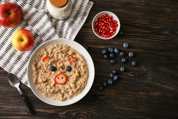 Plate with creative oatmeal for children on dark wooden table