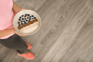 Woman holding plate with tasty oatmeal, sesame seeds and blueberries indoors