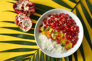 Tasty oatmeal with pomegranate seeds, succades and tropical leaf on color background