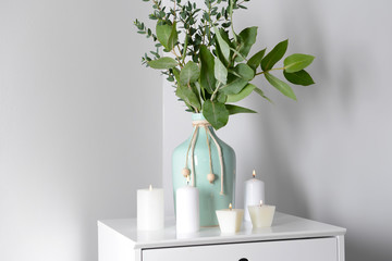 Burning candles and vase with eucalyptus branches on white table