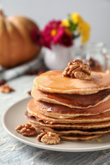 Stack of hot tasty pumpkin pancakes with honey and walnuts on plate