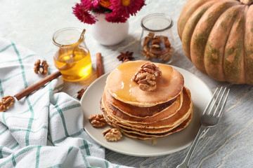 Stack of hot tasty pumpkin pancakes with honey and walnuts on plate