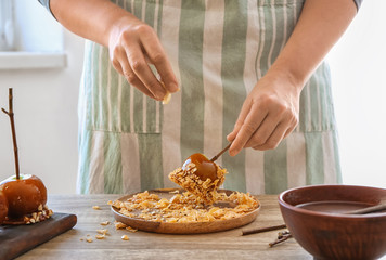 Woman rolling caramel apple in cornflakes at wooden table