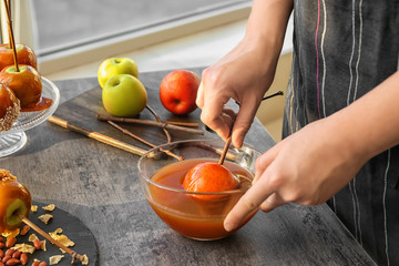 Woman dipping apple into glass bowl with caramel at grey table - obrazy, fototapety, plakaty