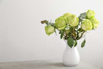 Vase with beautiful bouquet of green roses on table against light background