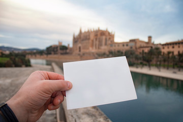White postcard mockup in man's hand on the background Catedral de Mallorca in Palma town on Mallorca Island in Spain.