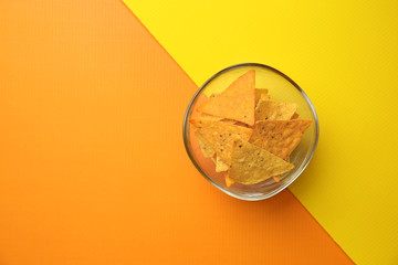 Bowl with tasty corn chips on color background