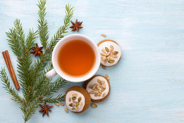 A cup of tea with fragrant honey Christmas gingerbreads with glaze and nuts, with Christmas tree branches and spices on a light blue background, free space, top view, horizontal