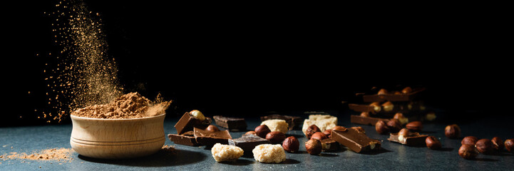 Cocoa powder in motion. Chocolate dust, cacao products, nuts on black background. Long web format