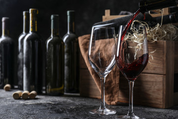 Pouring of red wine from bottle into glass on table