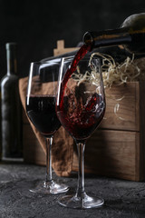 Pouring of red wine from bottle into glass on table