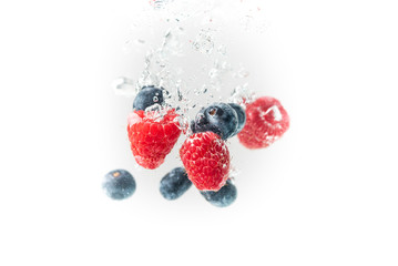 Blueberry’s and raspberries splashing into crystal clear water with air bubbles and sinking white background