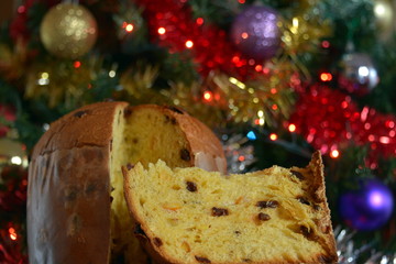 panettone tagliato, una fetta pronta da mangiare, sullo sfondo addobbi di natale