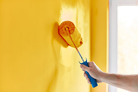 Male hand painting wall with paint roller. Painting apartment, renovating with sunflower color paint