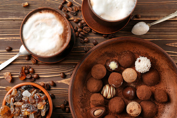 Fototapeta na wymiar Plate with tasty chocolate truffles and cups of cappuccino on wooden table