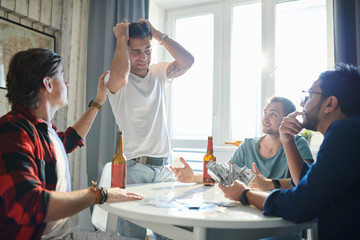 Upset young man lost in poker and didn't get his win with his friends comfort him at the table at home