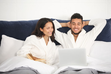 Fototapeta premium Young couple with laptop and book resting in bed