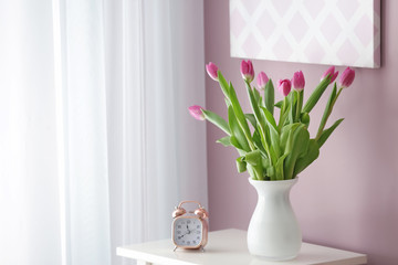 Vase with beautiful tulips and alarm clock on white table