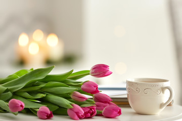 Beautiful tulips with cup of tea on white table