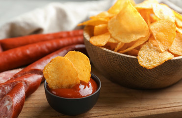 Tasty crispy potato chips with sauce and sausages on wooden board
