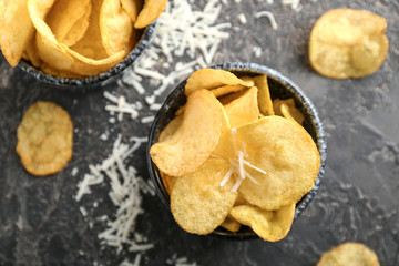 Bowls with tasty crispy potato chips on grey table