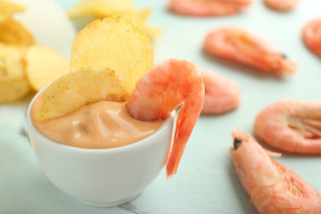 Tasty crispy potato chips in bowl with sauce and shrimps on light table