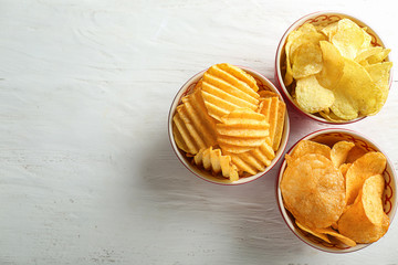 Bowls with tasty crispy potato chips on white wooden table