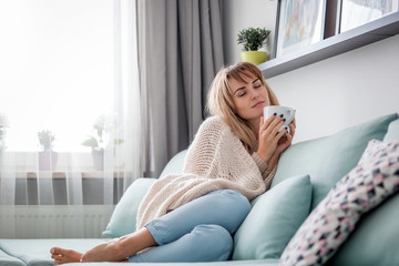 Obraz na płótnie Canvas Happy woman in soft sweater relaxing at home with cup of hot tea or coffee