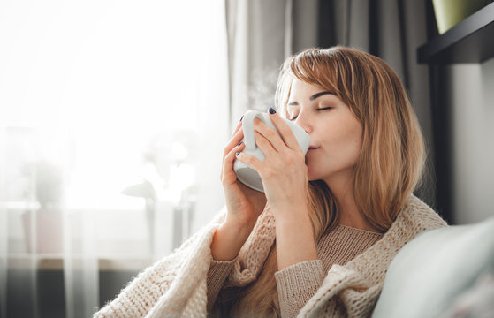 Happy Woman In Soft Sweater Relaxing At Home With Cup Of Hot Tea Or Coffee