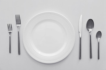 Plate and set of cutlery on white background, flat lay