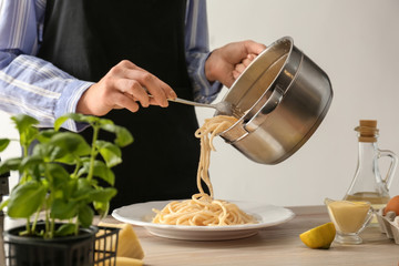 Woman putting delicious pasta onto plate in kitchen